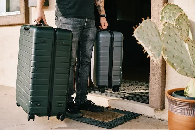 man in black denim jeans and black leather shoes standing beside black luggage bag - Travel Tips Before Heading to Airports